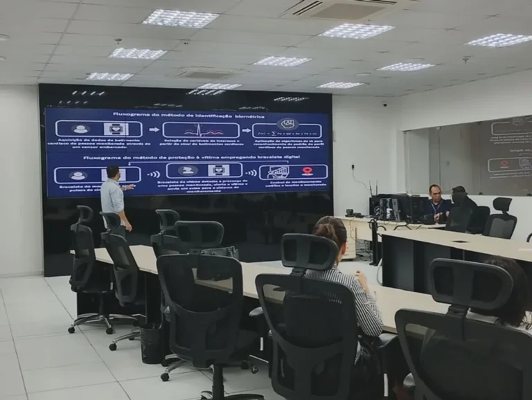Tela de monitoramento de centro de comando e controle exibindo imagens de câmeras de segurança e dados em tempo real, com equipes de segurança no fundo.