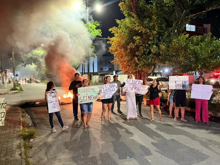 Moradores protestam em rua alagada em João Pessoa, com fogo em pneus sendo apagado pela polícia