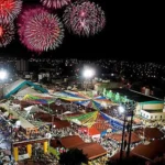 Vista aérea do Parque do Povo em Campina Grande durante o São João, com barracas, decorações e grande público, simbolizando a movimentação econômica da festa.
