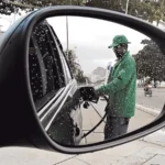 Bico de bomba de combustível abastecendo um carro com preços variados ao fundo.