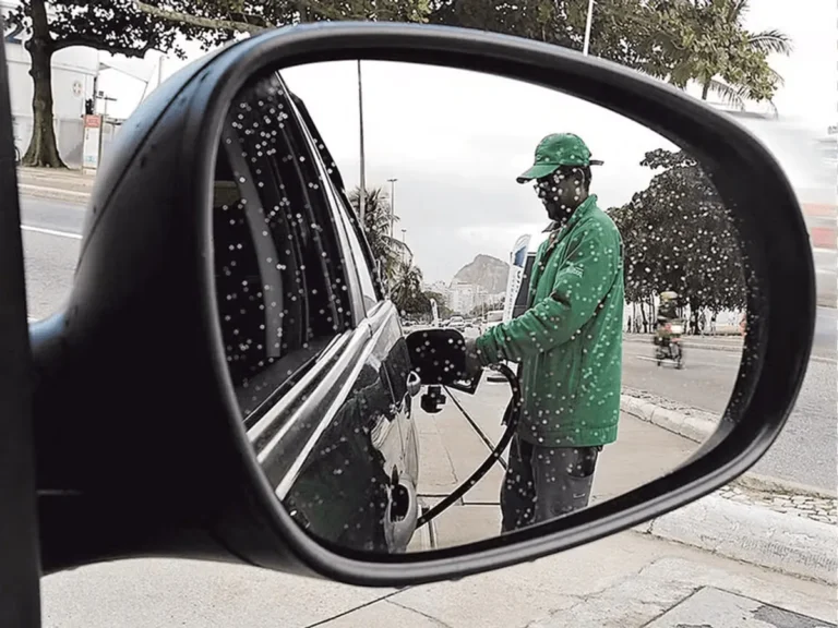 Bico de bomba de combustível abastecendo um carro com preços variados ao fundo.