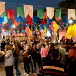 Pessoas celebrando o São João em uma rua decorada com bandeirinhas e fogueiras no Nordeste brasileiro, com músicos e comidas típicas.