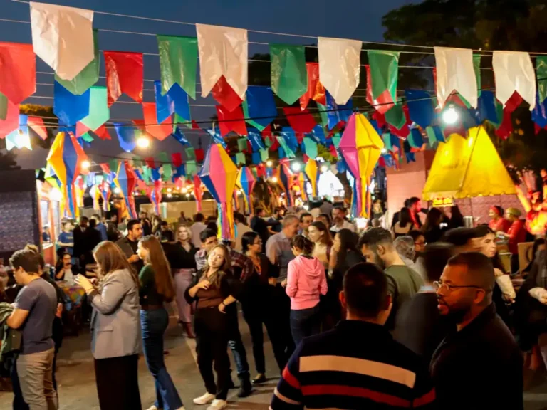 Pessoas celebrando o São João em uma rua decorada com bandeirinhas e fogueiras no Nordeste brasileiro, com músicos e comidas típicas.
