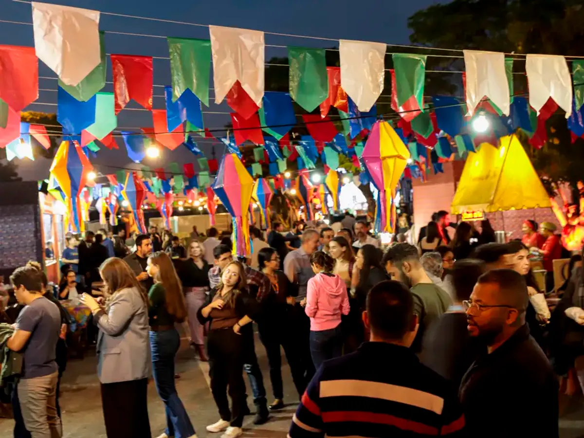 Pessoas celebrando o São João em uma rua decorada com bandeirinhas e fogueiras no Nordeste brasileiro, com músicos e comidas típicas.