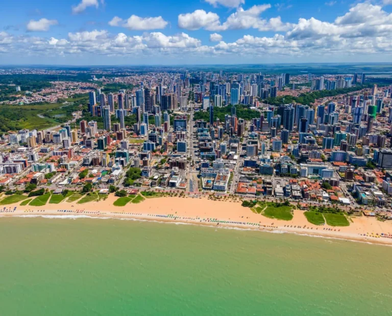 Vista panorâmica aérea da orla de João Pessoa ao amanhecer, destacando praias, mar e a cidade em desenvolvimento.