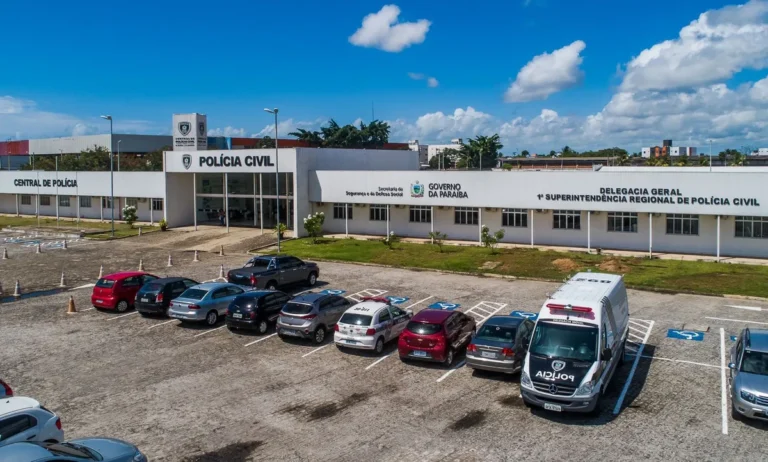 Policiais da Polícia Civil da Paraíba em operação em João Pessoa, com viatura ao fundo.