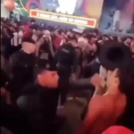 Policial militar em evento público noturno, com expressão séria.