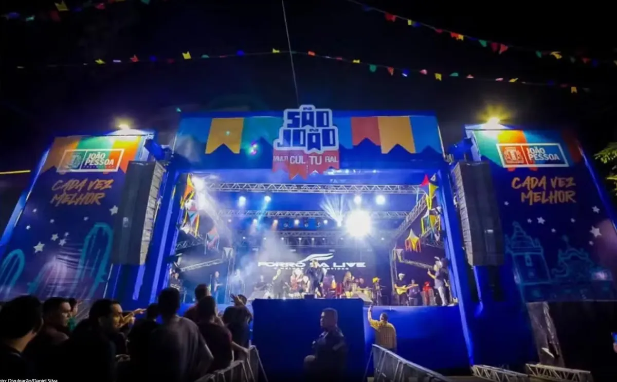 Prefeito de João Pessoa anunciando realocação de verbas do São João para vítimas das chuvas, com palco junino ao fundo