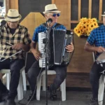 Trio de forró se apresentando na entrada do SESI Museu Digital durante celebrações juninas.
