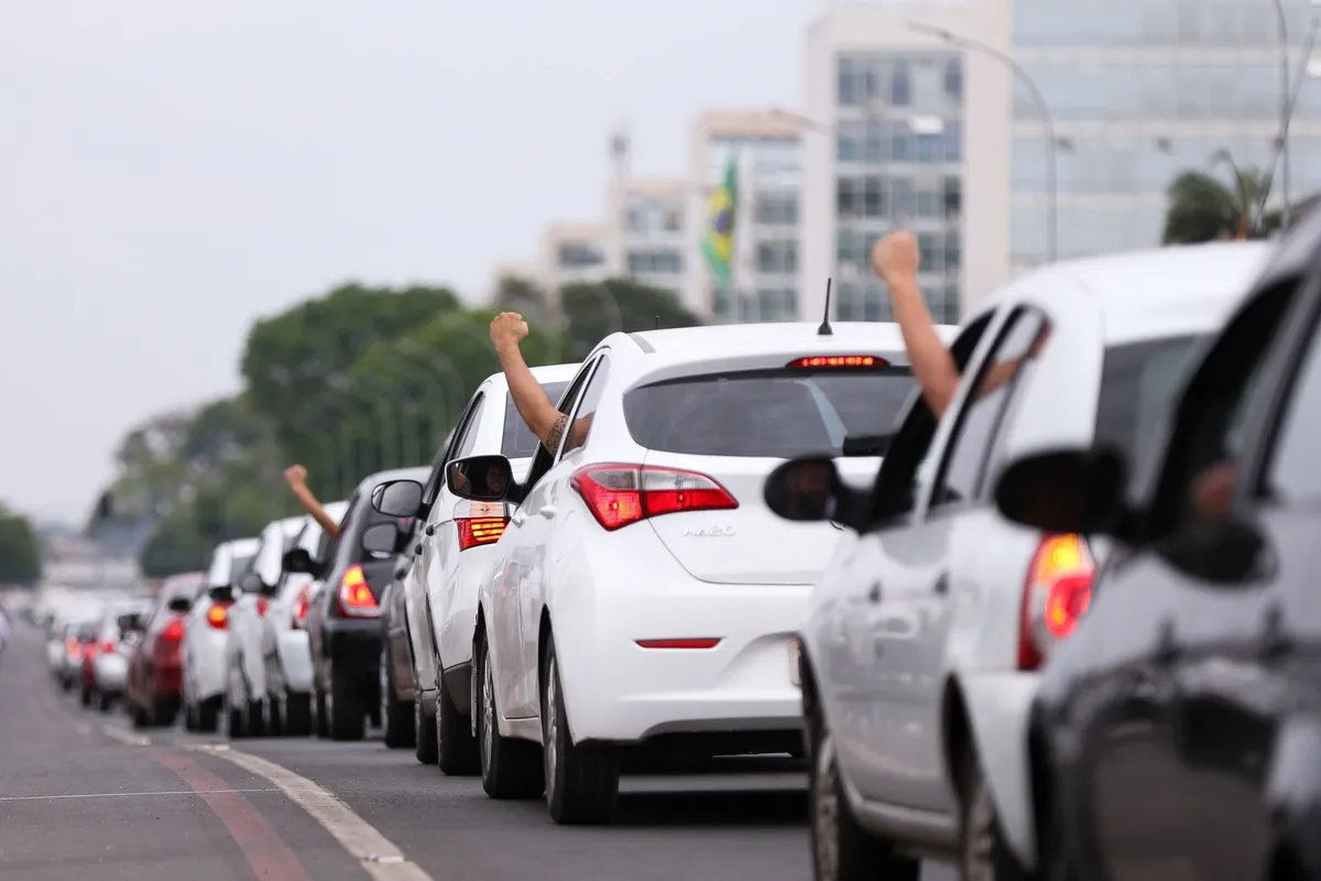Fiscal eleitoral aponta para adesivo de propaganda em carro de aplicativo, indicando irregularidade.